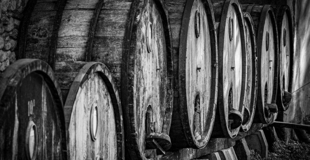 A row of vintage wooden wine barrels in a cellar, showcasing rustic textures in monochrome.